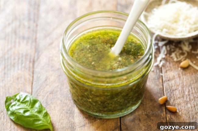 Close-up of fresh basil pesto in a small jar with a white spoon