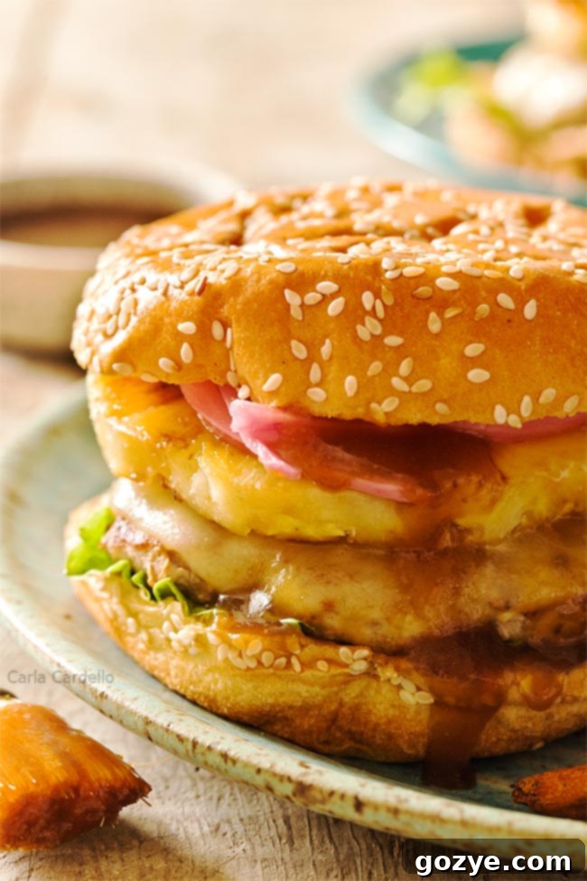 Savory Teriyaki Turkey Burgers 3 A close-up shot of a Teriyaki Turkey Burger, showcasing the perfectly melted Swiss cheese, golden-brown grilled pineapple slice, and vibrant pickled red onion, all drizzled with pineapple teriyaki sauce.