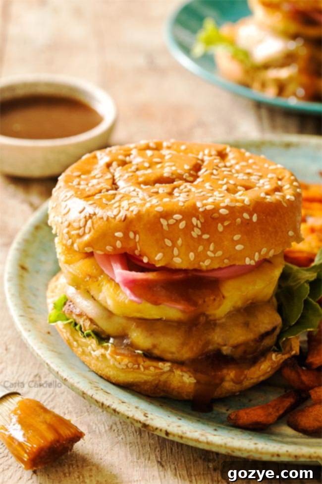 Savory Teriyaki Turkey Burgers 4 A perfectly assembled Teriyaki Turkey Burger with grilled pineapple, pickled red onion, and melted Swiss cheese, served on a bun with sweet potato fries in the background.