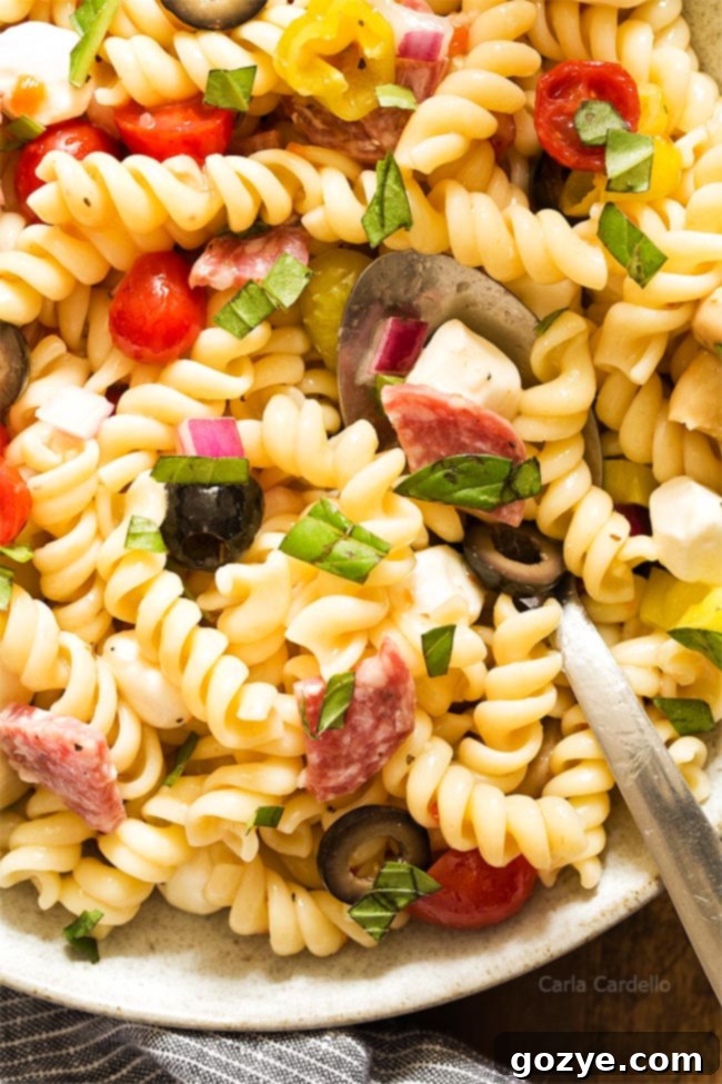 Close-up shot of Antipasto Pasta Salad with a serving spoon, showcasing the delicious ingredients