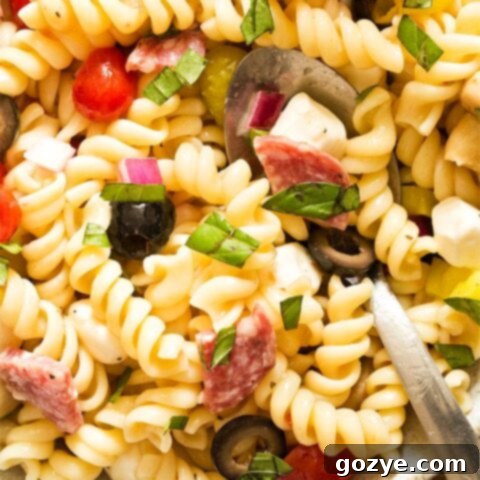 Close up photo of Antipasto Pasta Salad in a bowl with a serving spoon, garnished with fresh basil