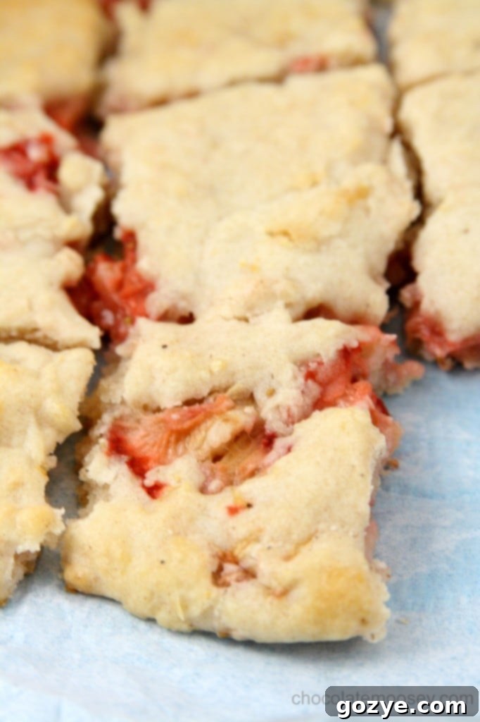 Hands gently working with sticky biscuit dough on a floured surface, with strawberry pieces visible