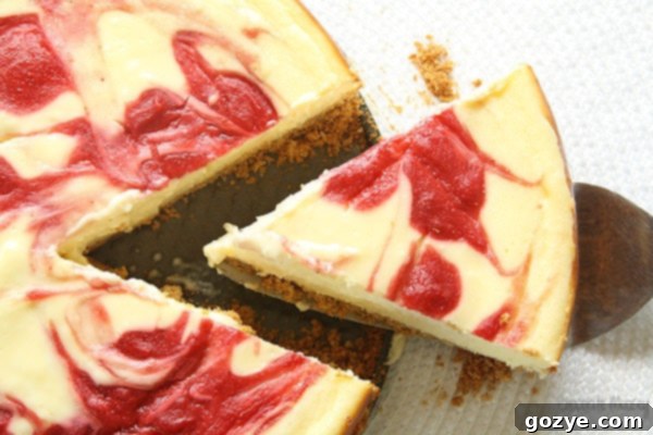 A hand gently removing a slice of strawberry swirl cheesecake from the whole cake with a cake cutter.