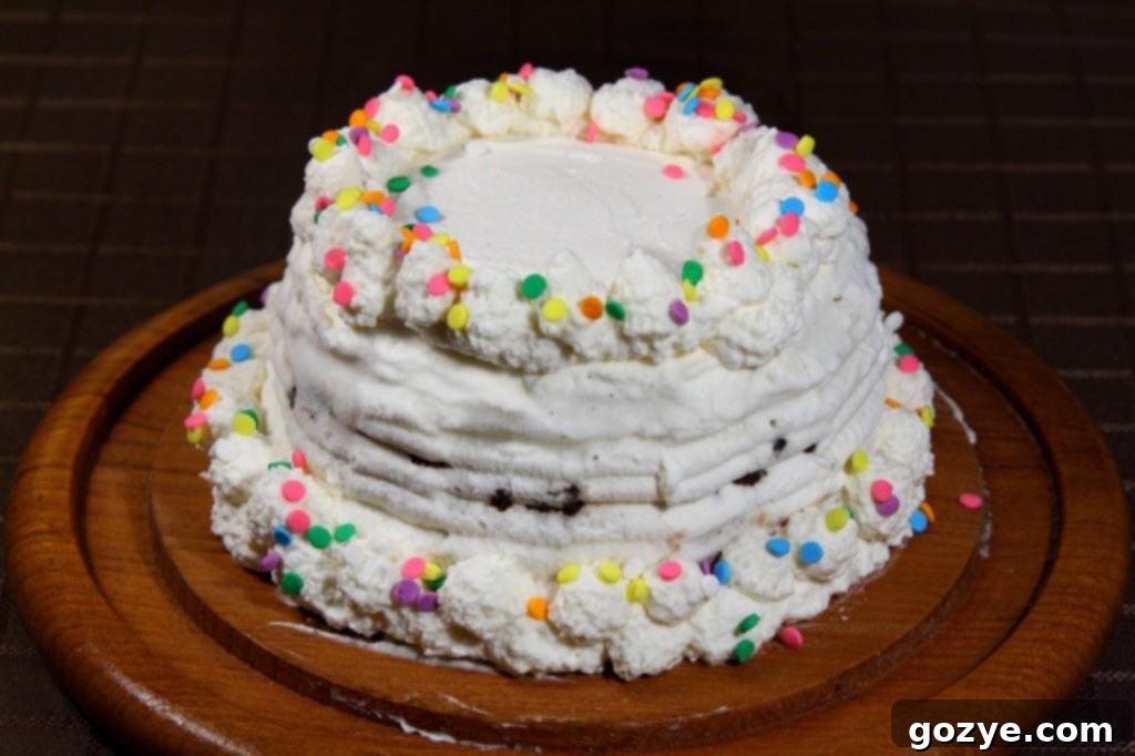 Hand decorating a homemade Copycat Dairy Queen Ice Cream Cake with fluffy whipped cream and colorful sprinkles