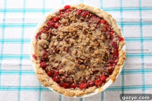 Close-up shot of a whole Cinnamon Pecan Cherry Crumble Pie, showcasing its golden-brown streusel and bubbly cherry filling.