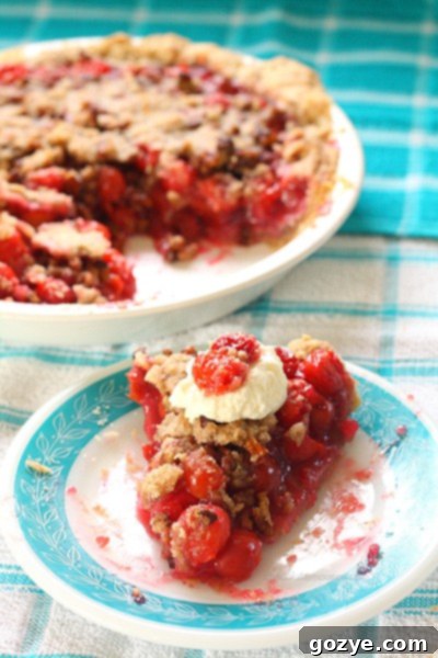 The full baked Cherry Crumble Pie in a ceramic dish, with a section already removed, showcasing the generous streusel topping.