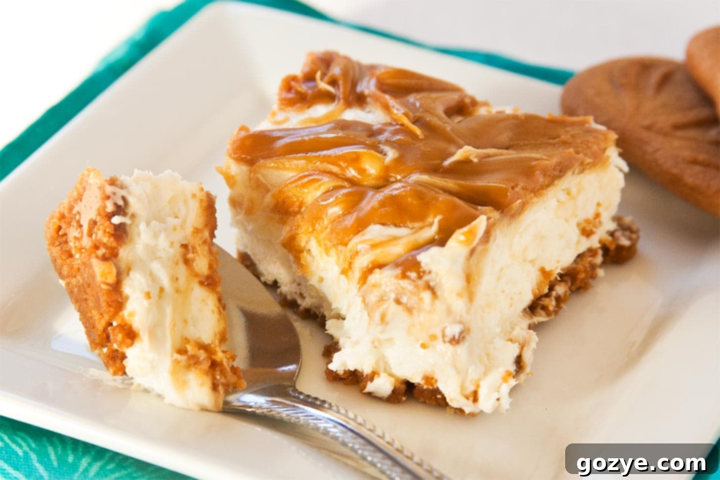 A beautifully presented slice of No Bake Biscoff Cheesecake on a white plate with a spoon, ready to be enjoyed