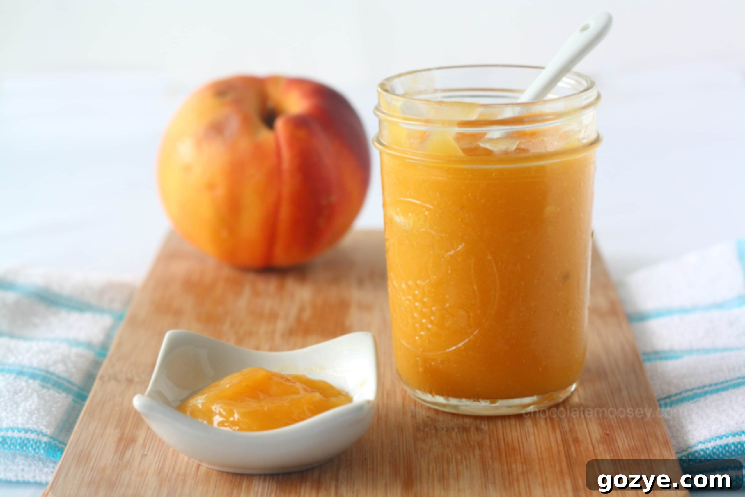 Jar of peach curd on a rustic cutting board with fresh peaches in the background