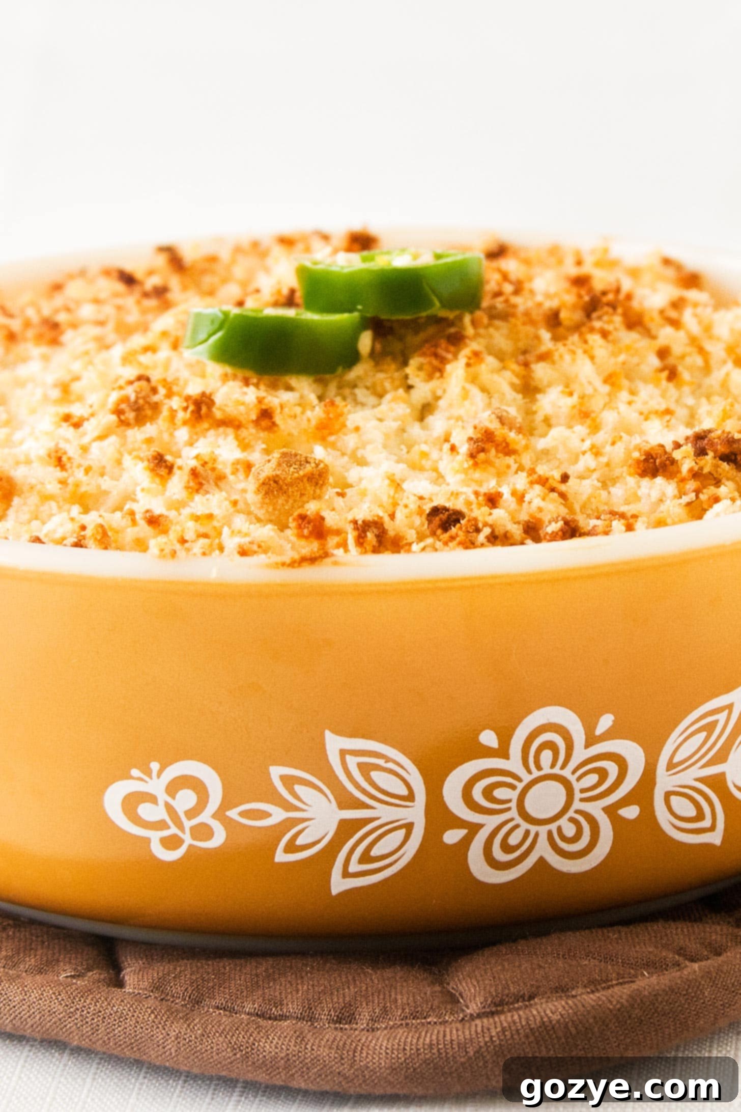 Close up shot of golden and bubbly jalapeno popper dip in a yellow casserole dish.