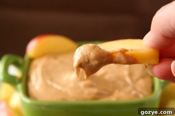 Dippable Caramel Apple Cheesecake 5 A close-up of an apple slice being dipped into the rich caramel apple cheesecake dip