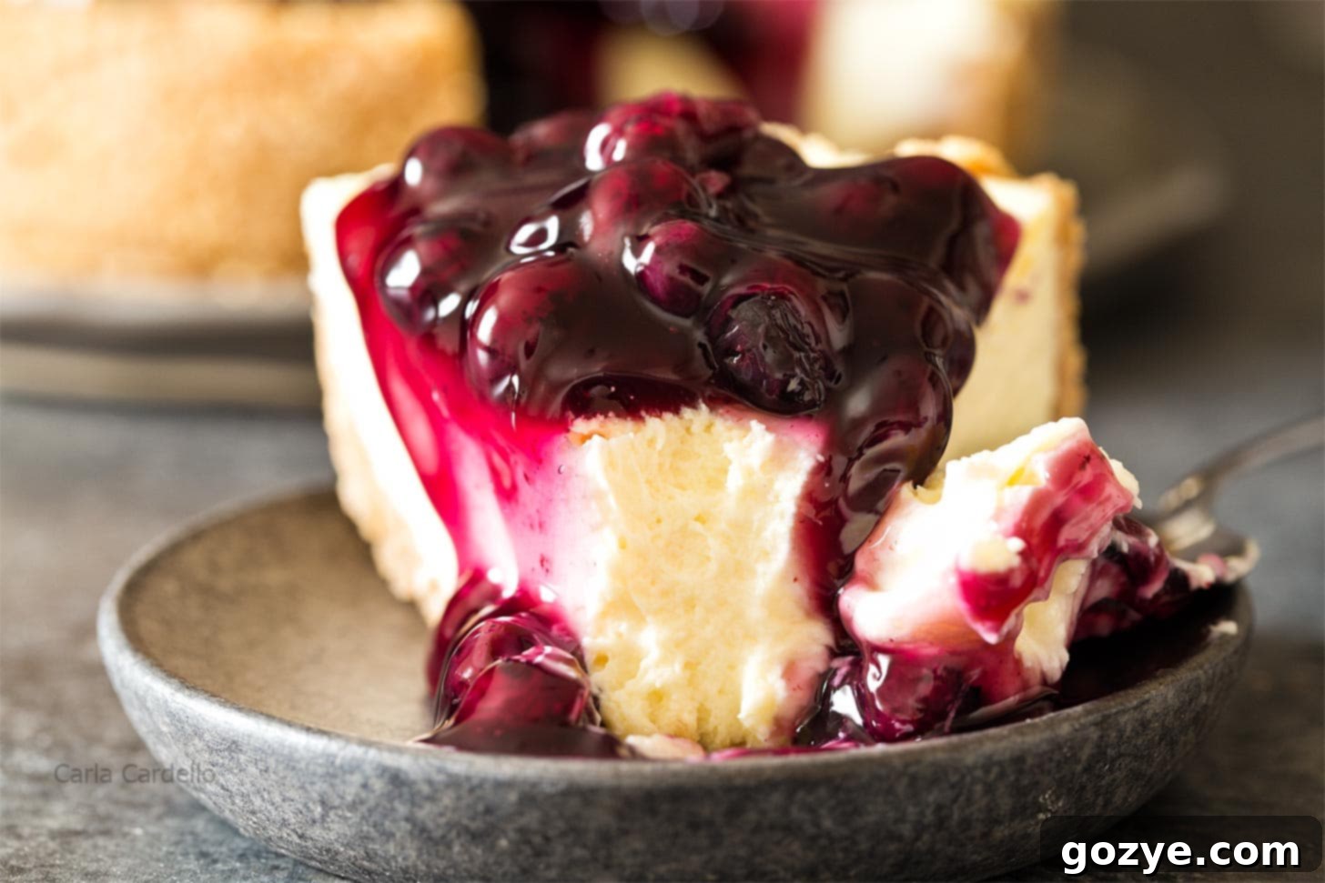 A second close-up view of a slice of 7 inch cheesecake with blueberry pie filling and whipped cream, highlighting its texture.