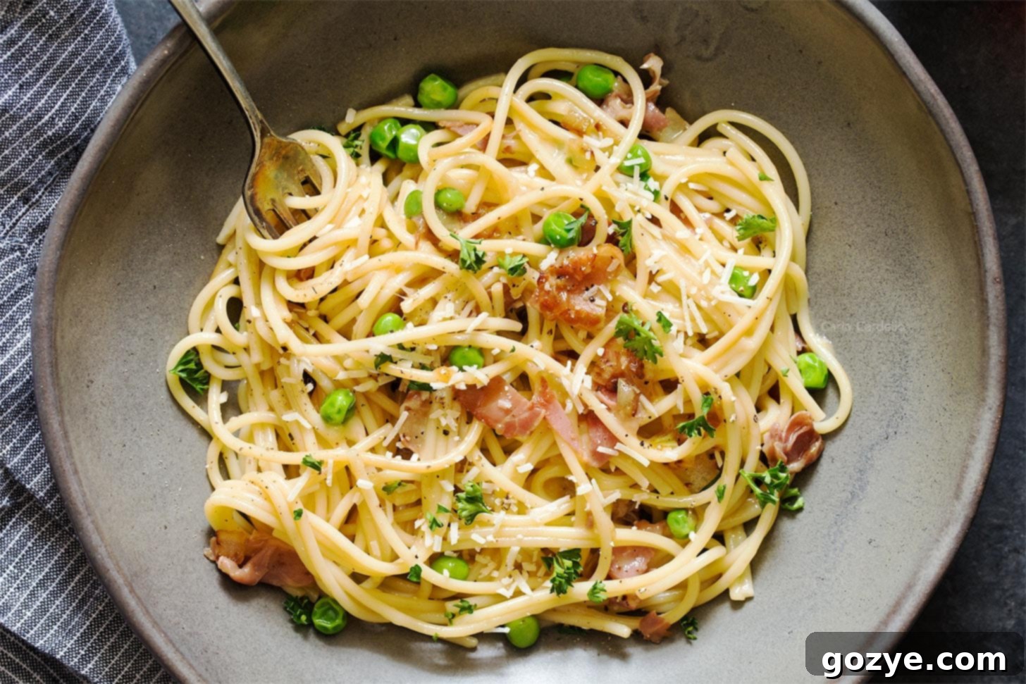 Close up of pasta with prosciutto and peas in grey bowl with fork