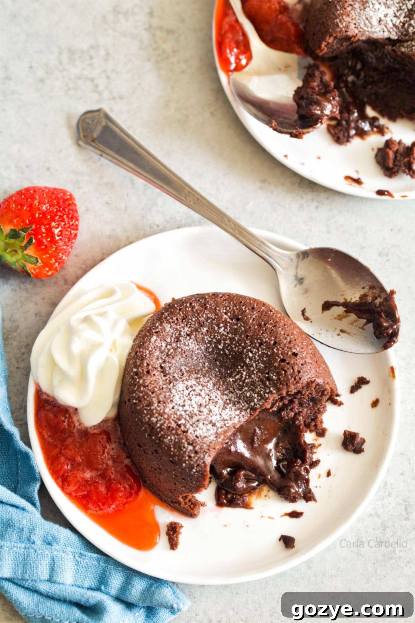 Two mini lava cakes on plates with whipped cream and strawberry sauce