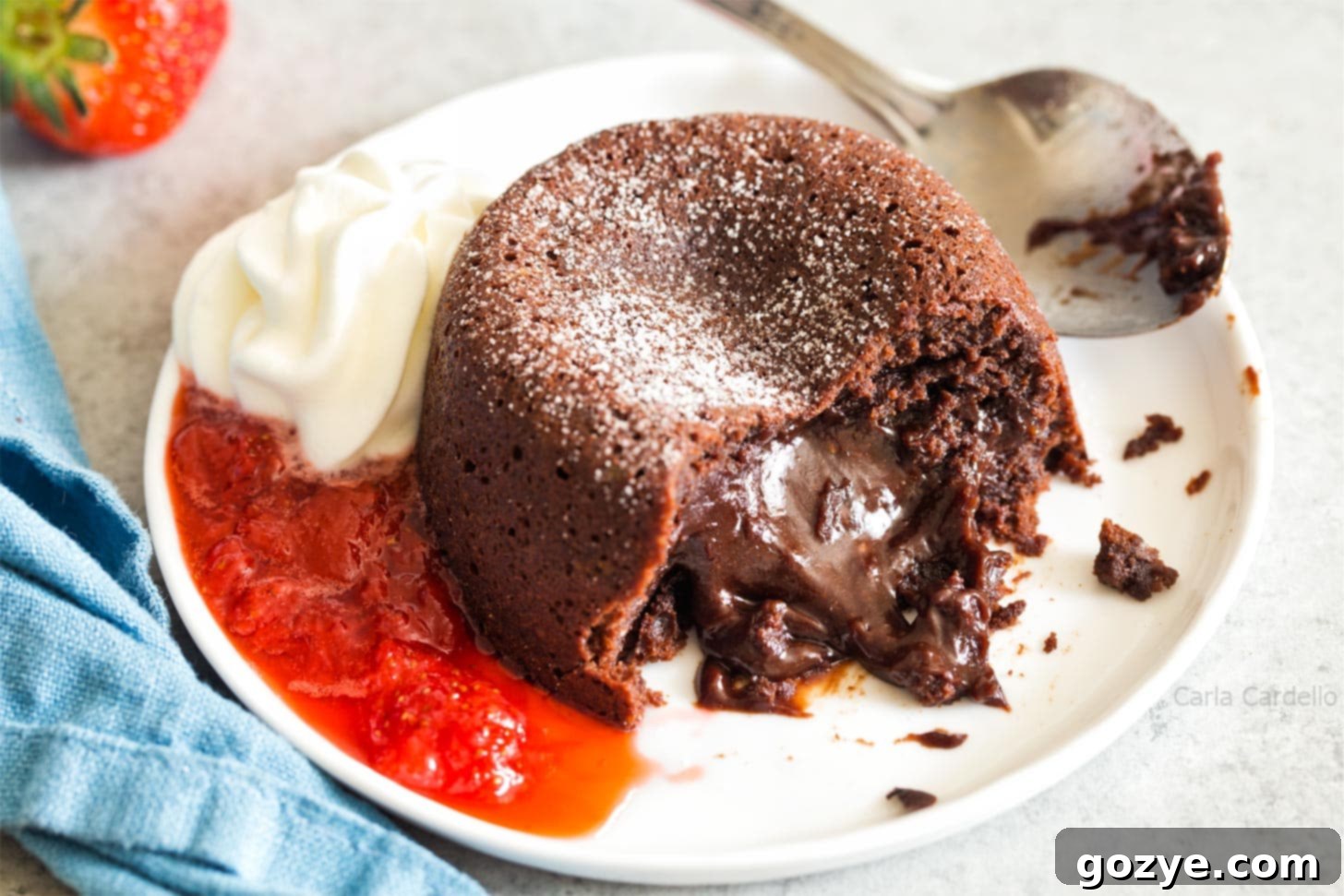 Mini Molten Chocolate Cake oozing out onto plate with whipped cream and strawberry sauce
