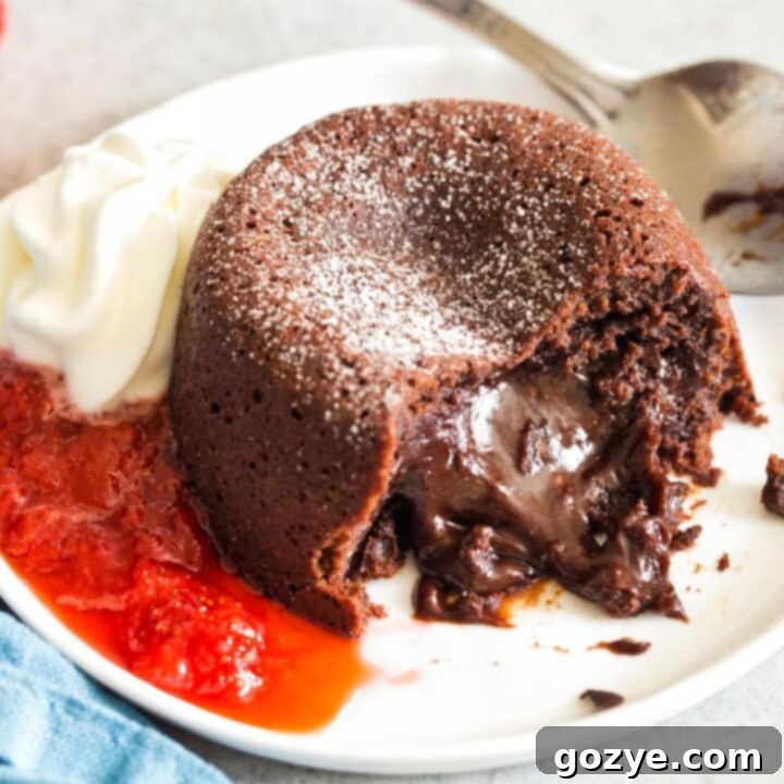 Mini Molten Chocolate Cake oozing out onto plate with whipped cream and strawberry sauce