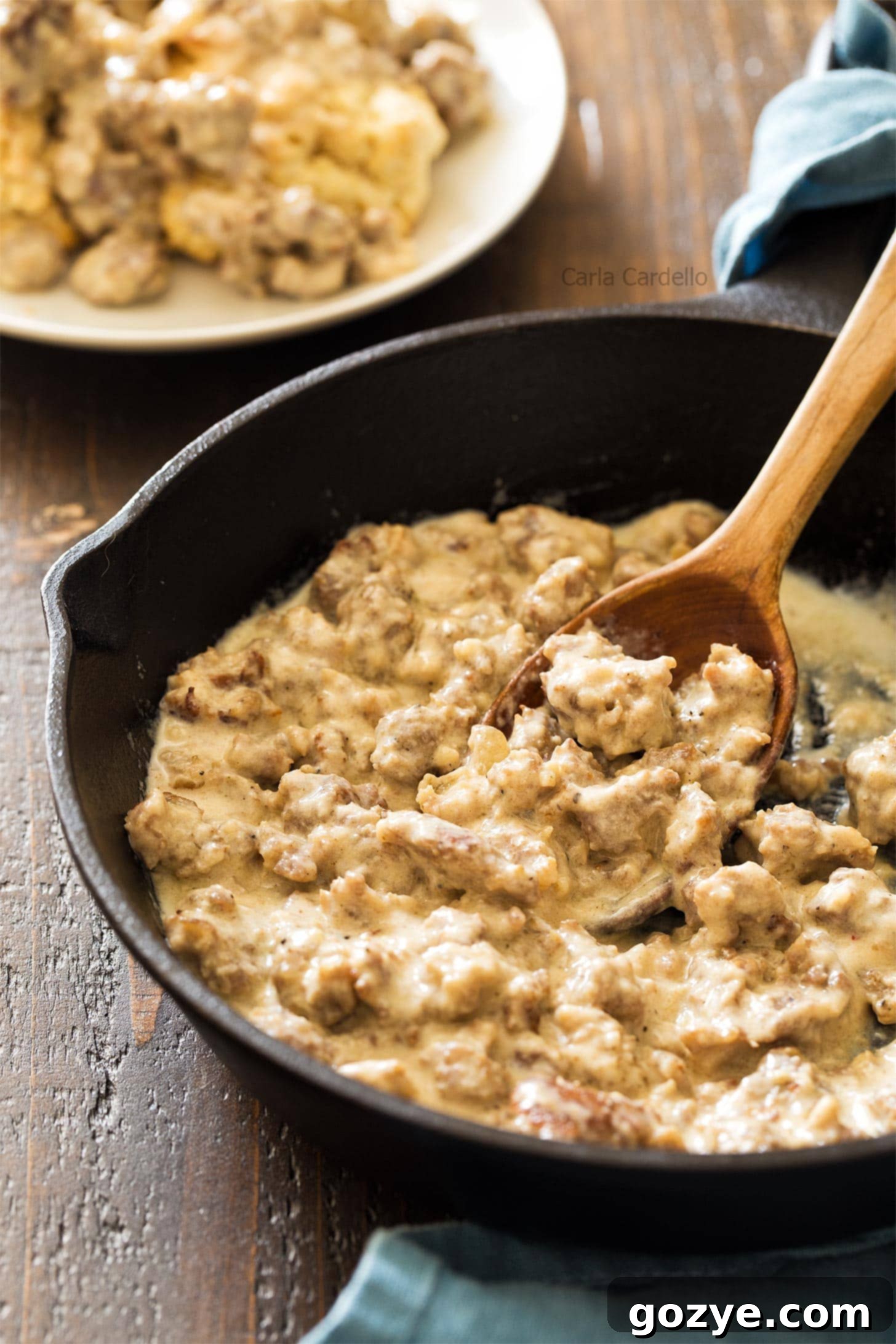 Sausage gravy with wooden spoon in cast iron skillet, showcasing its rich texture