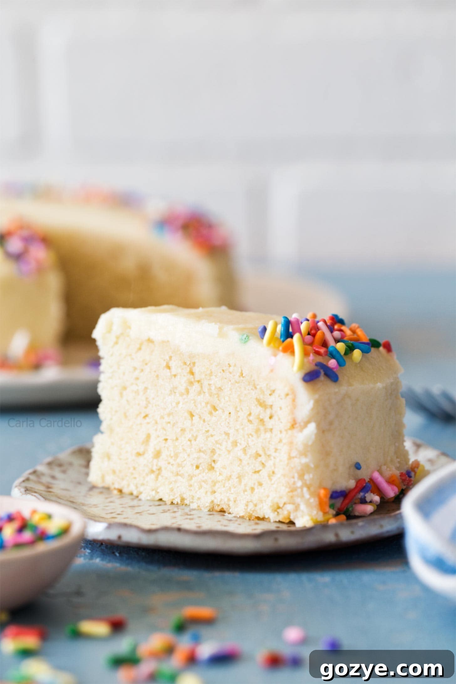 Slice of small vanilla cake on a white plate, showing its tender crumb and a generous layer of creamy frosting.