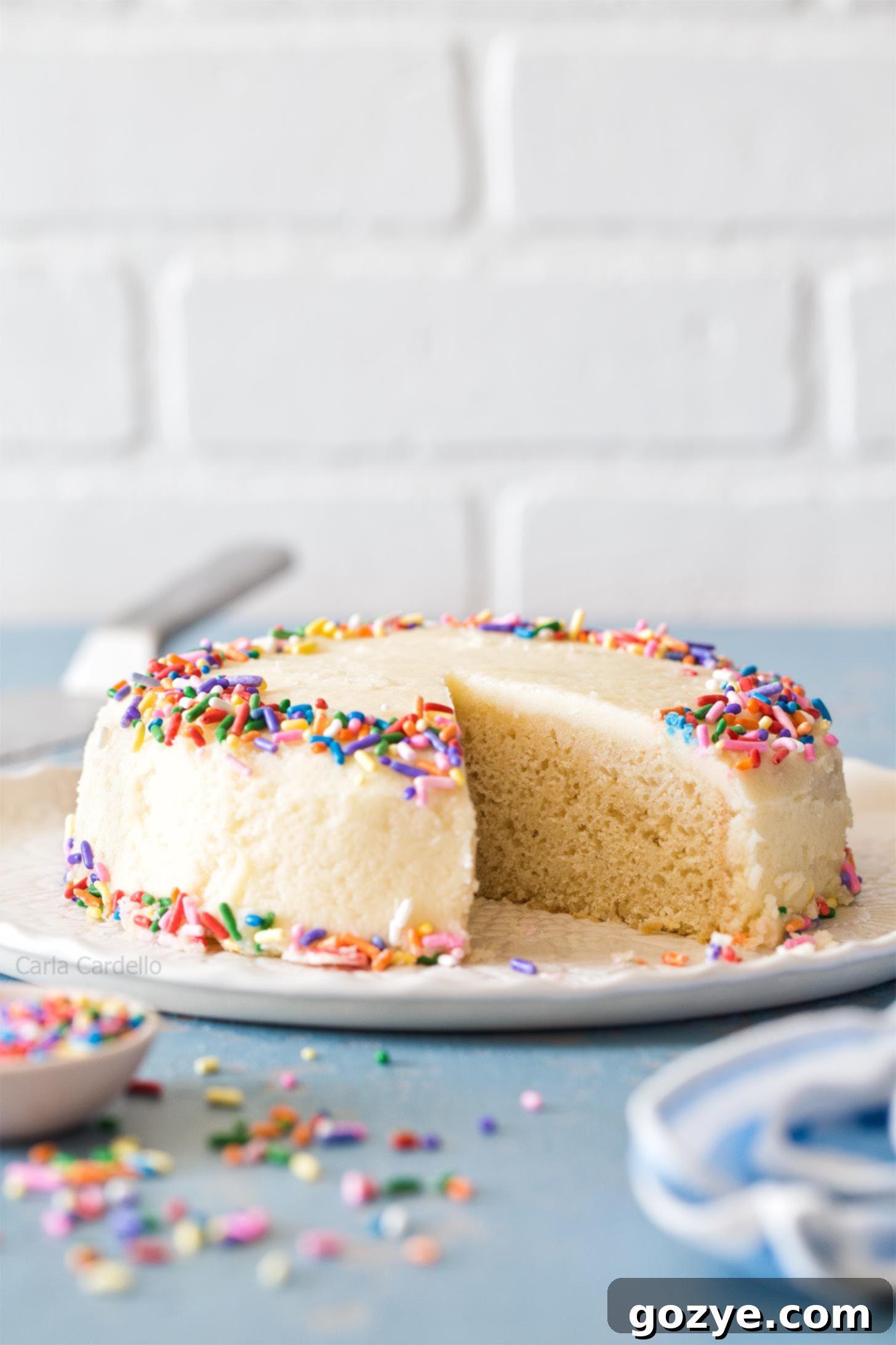 A beautifully frosted small vanilla cake on a pristine white plate, ready to be served.