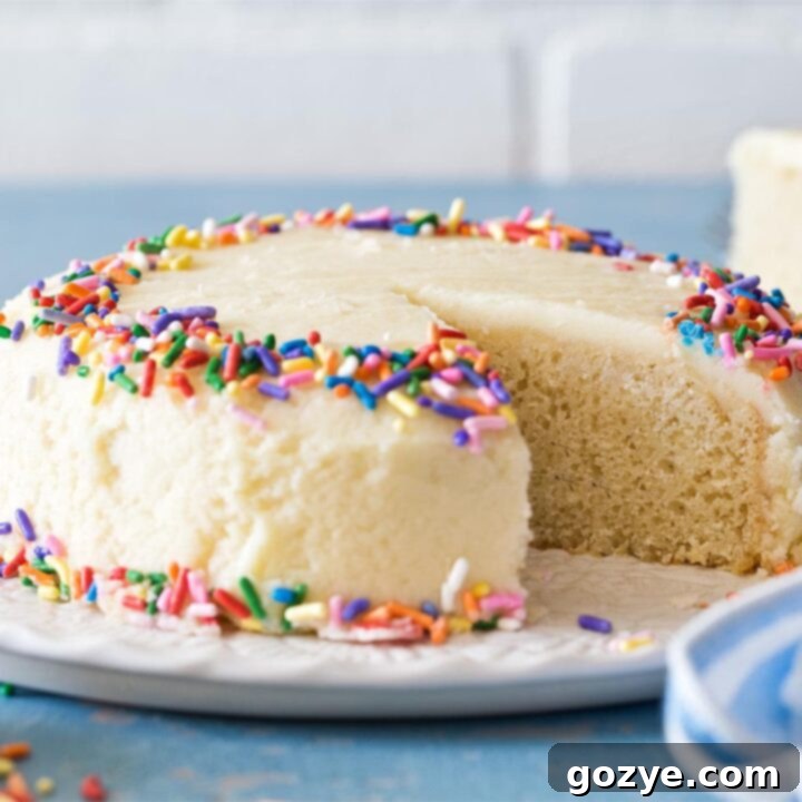 6 inch vanilla cake on white platter, with a delicate slice showing its perfect texture and frosting.