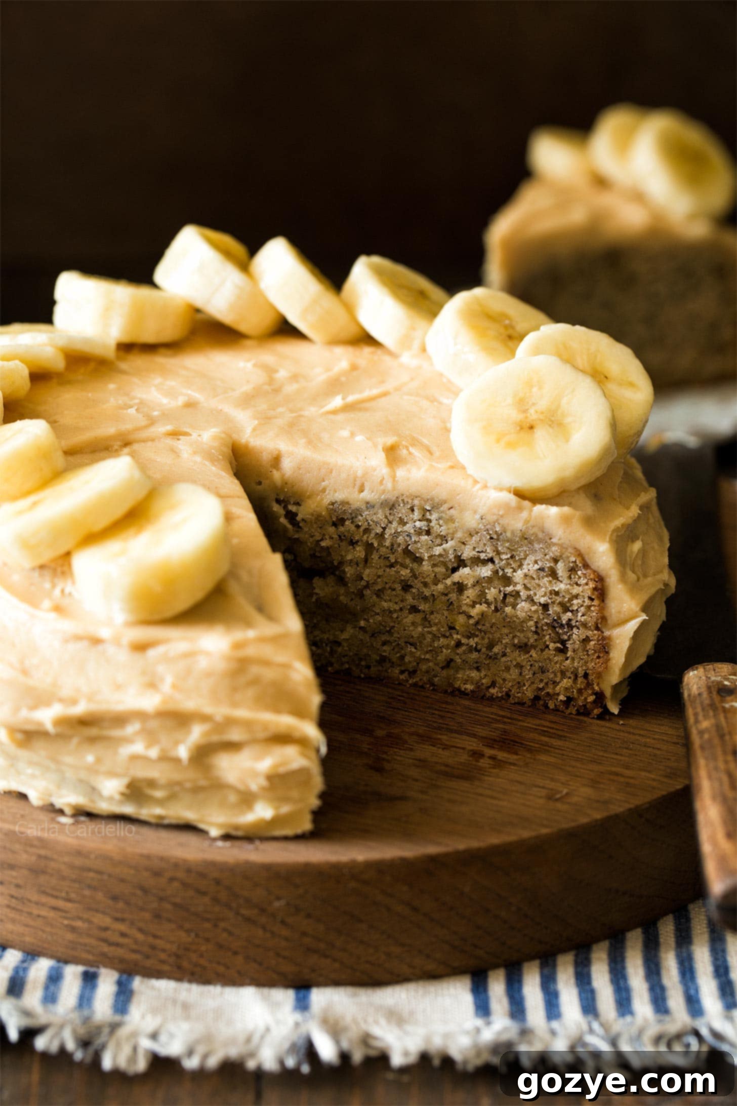 Small Banana Cake on wooden board with slice cut out, showcasing its moist texture and creamy frosting
