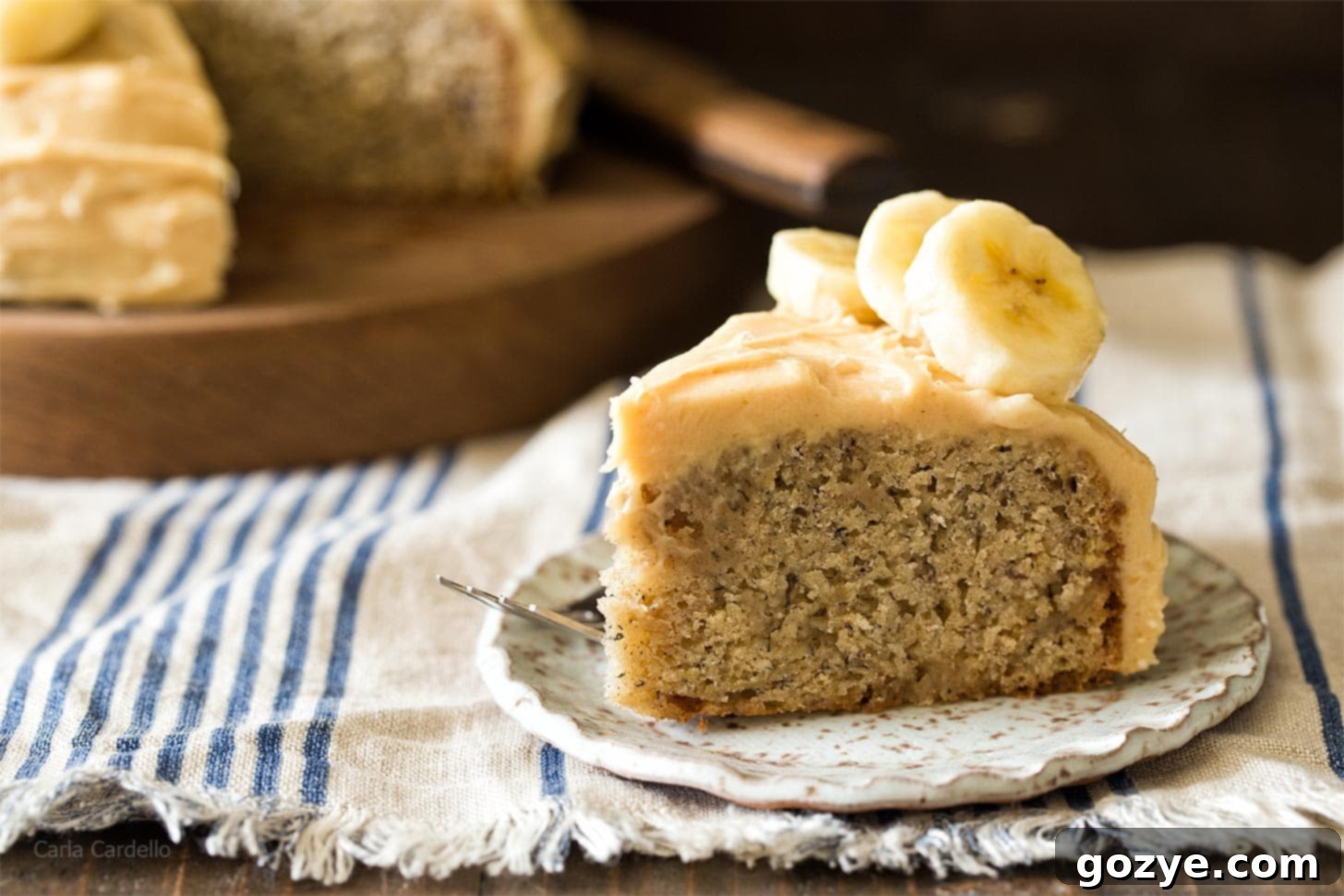 Close-up of a slice of banana cake with cream cheese frosting on a plate, highlighting the delicious layers