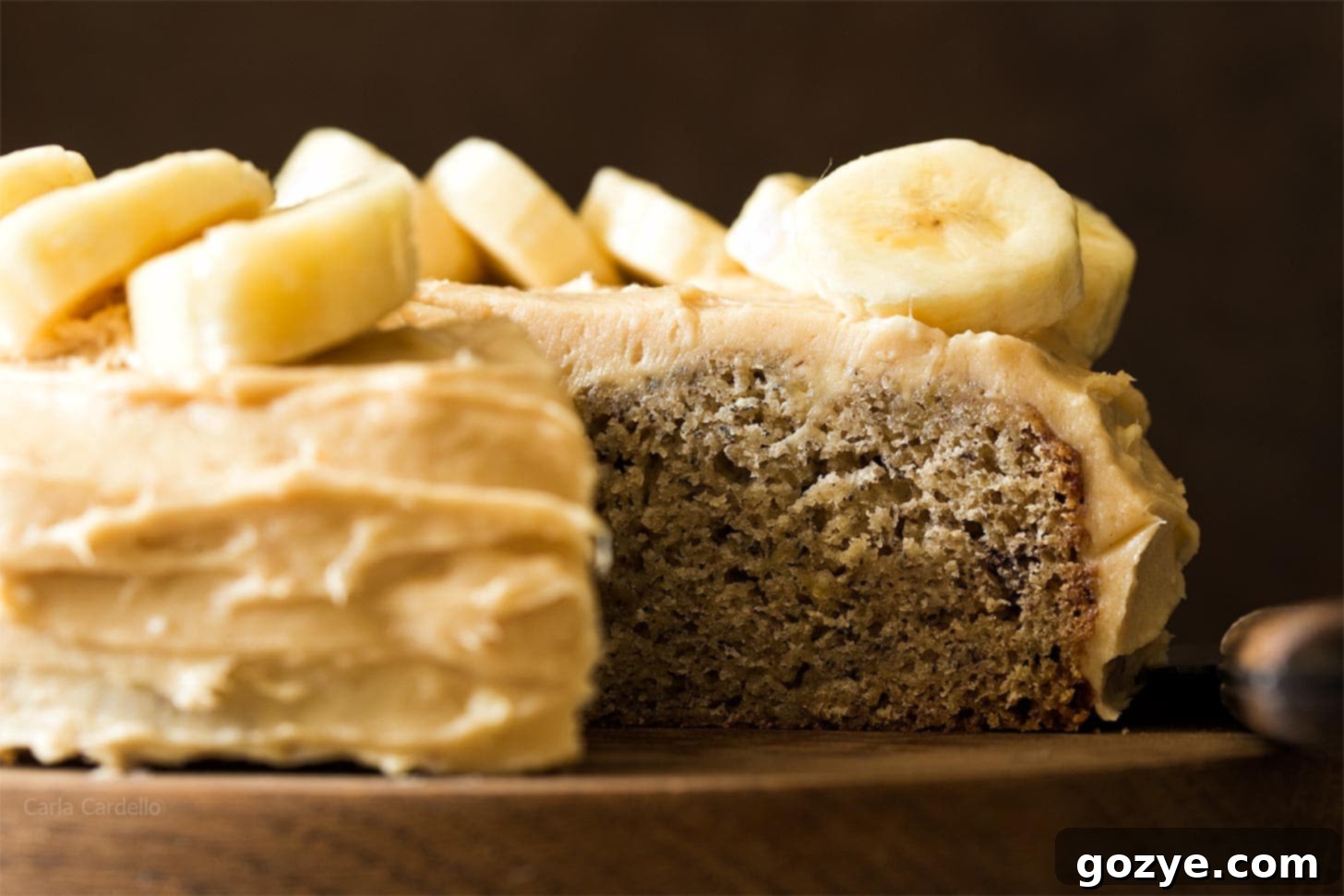 A small banana cake, artfully cut to reveal its moist interior, sitting on a wooden board
