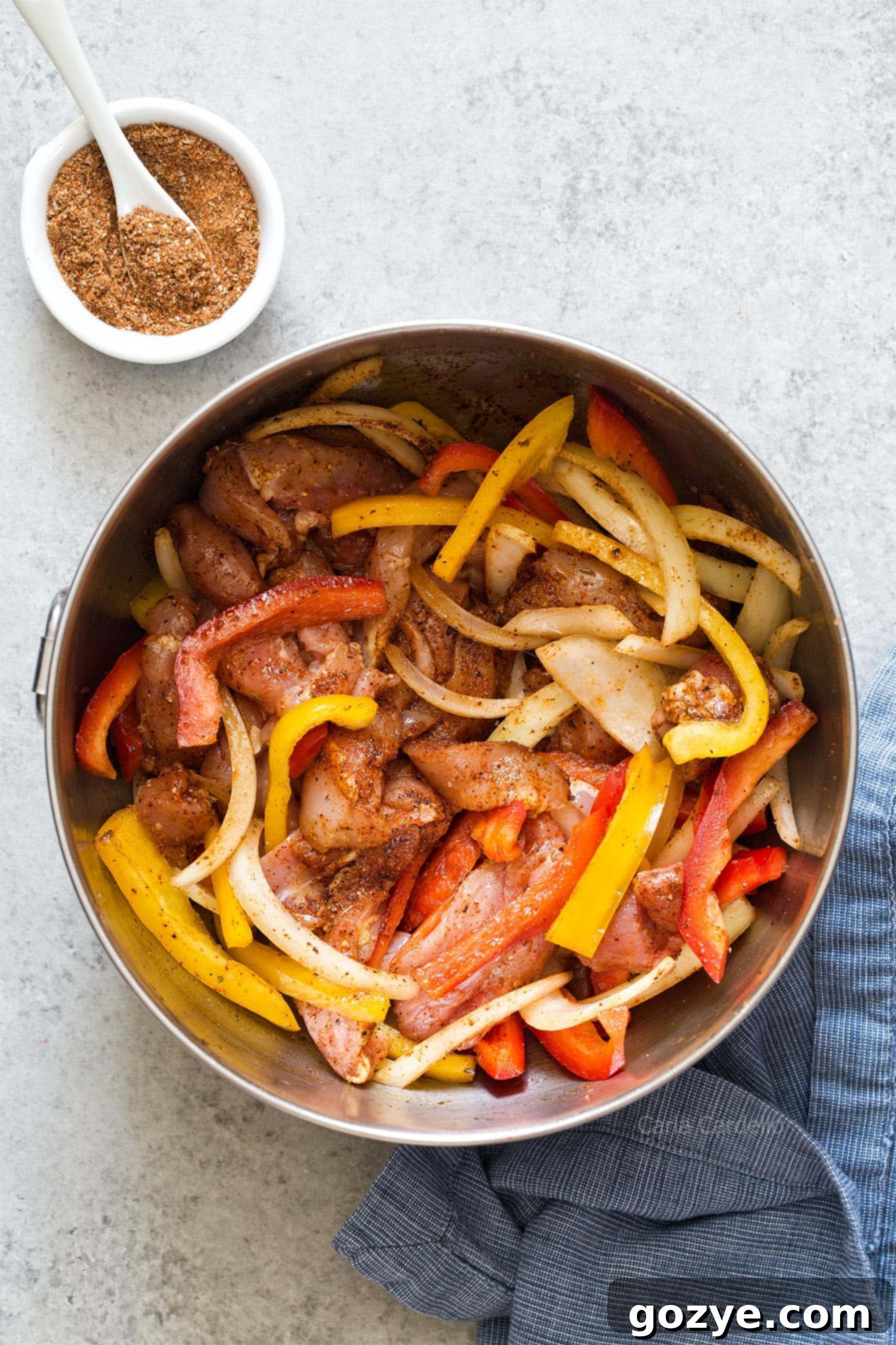 Chicken, bell pepper, and onion in a bowl, coated with olive oil and fajita seasoning