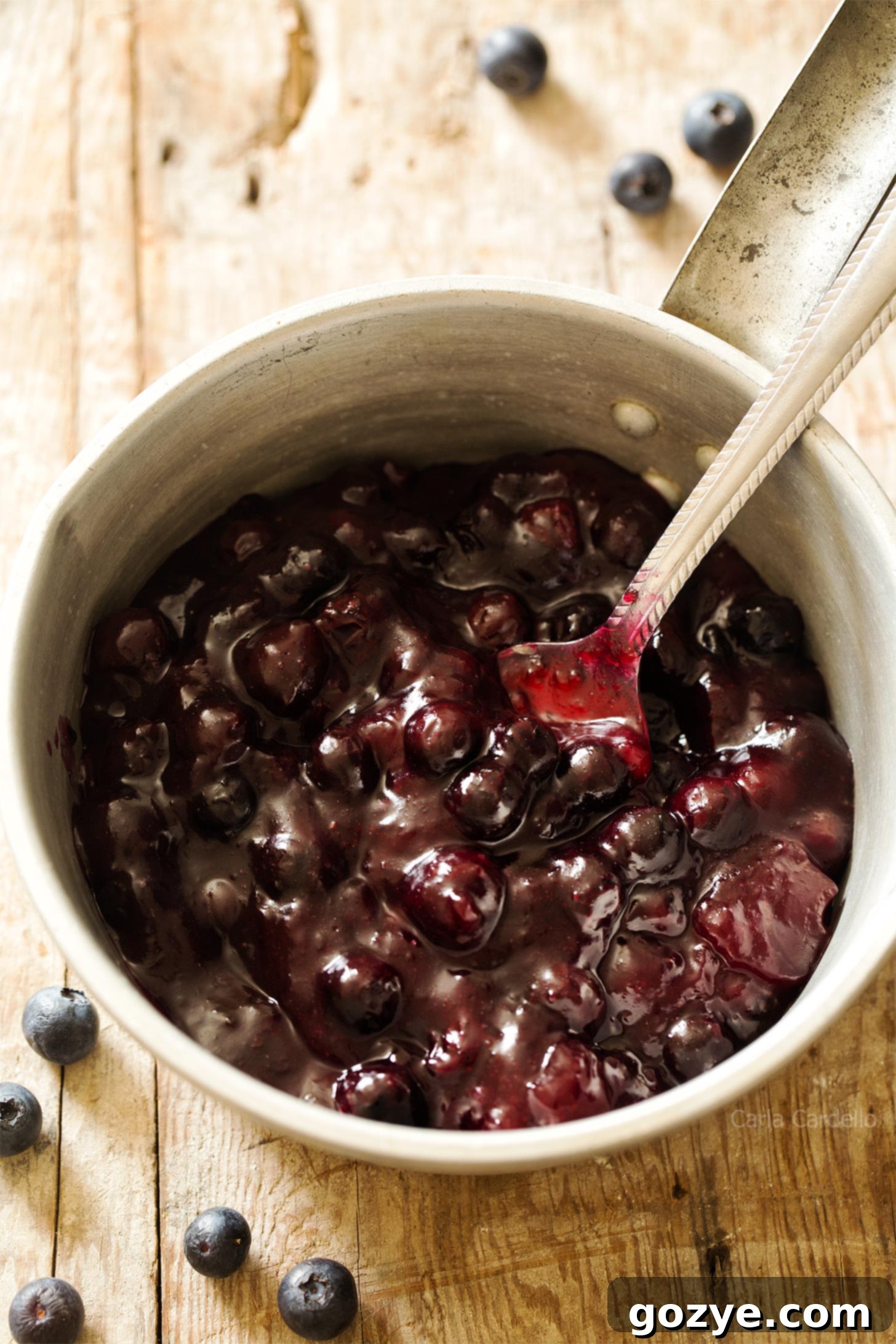 Fresh homemade blueberry pie filling simmering in a saucepan with a spoon resting in it