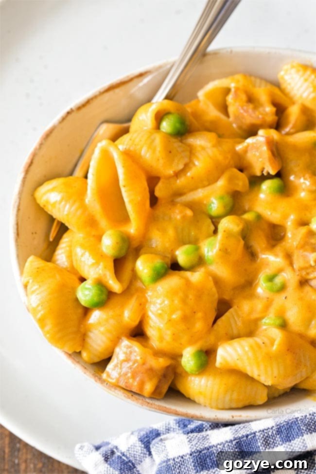 Close up of pumpkin mac and cheese, showing creamy texture and bits of sausage and peas.