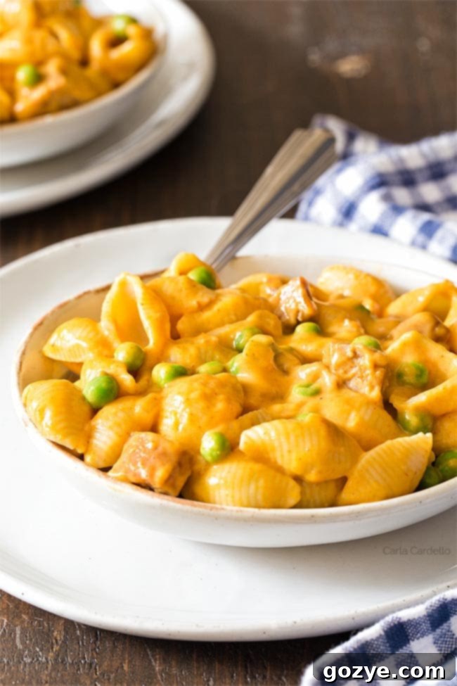 A white bowl filled with pumpkin mac and cheese, garnished with fresh herbs, on a white plate.