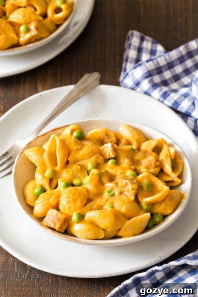 Pumpkin macaroni and cheese in a white bowl with a fork, ready to be eaten.