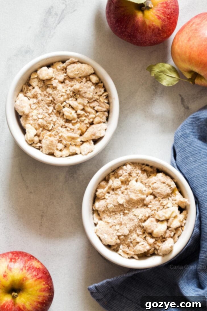 Unbaked apple crisps in ramekins, topped with a generous layer of streusel, ready for the oven
