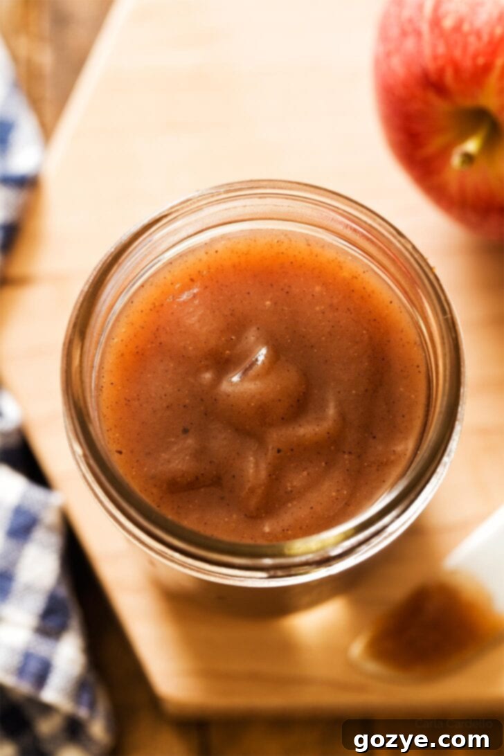 Close up shot of a glass jar filled with rich, dark apple butter, highlighting its smooth texture.