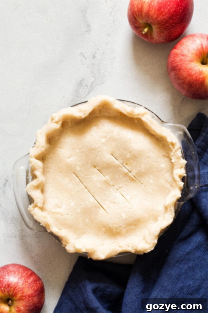 An unbaked 6-inch apple pie, topped with a decorative crust and egg wash, ready for the oven.
