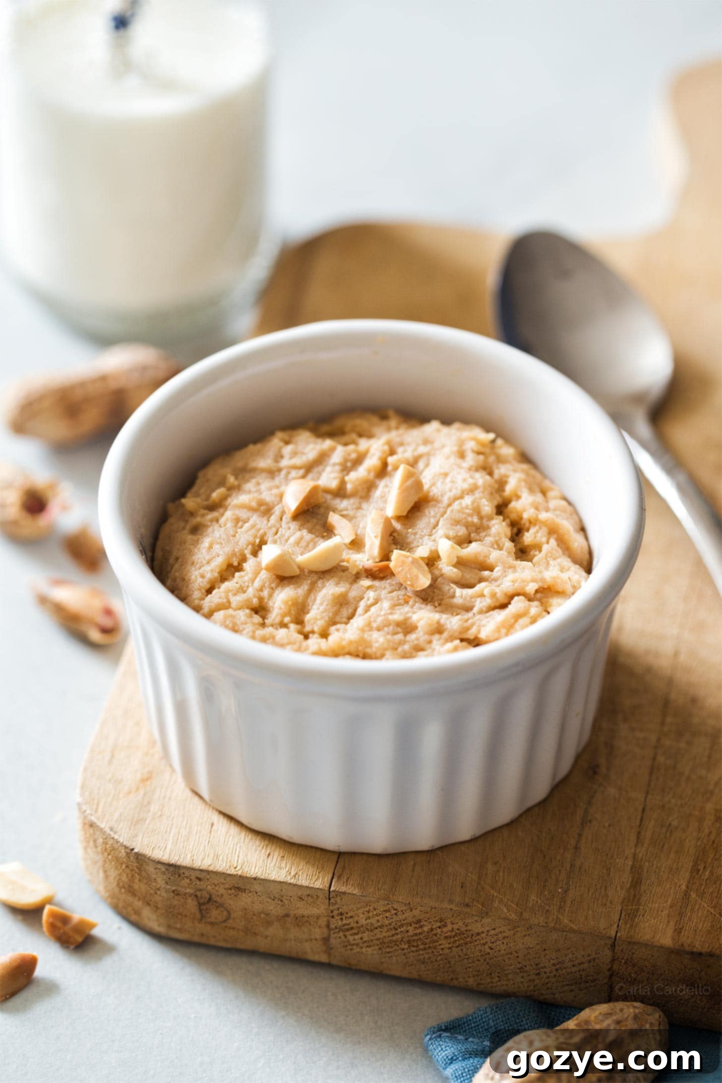 Perfectly baked microwave peanut butter cookie in a white ramekin, resting on a rustic wooden cutting board, ready to be enjoyed.