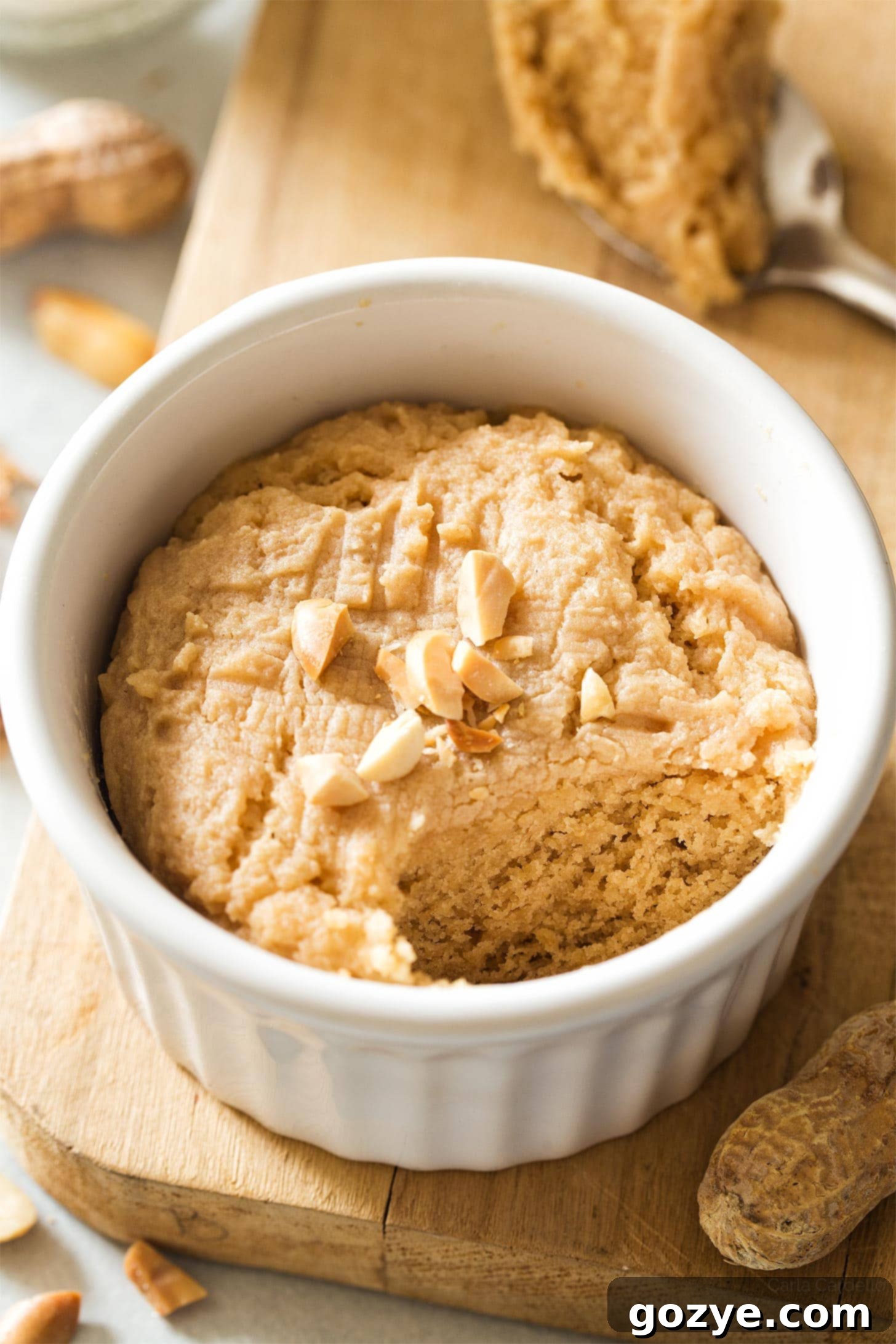 Close-up view of a freshly microwaved peanut butter cookie in a white ramekin, with a classic fork criss-cross pattern and inviting texture.