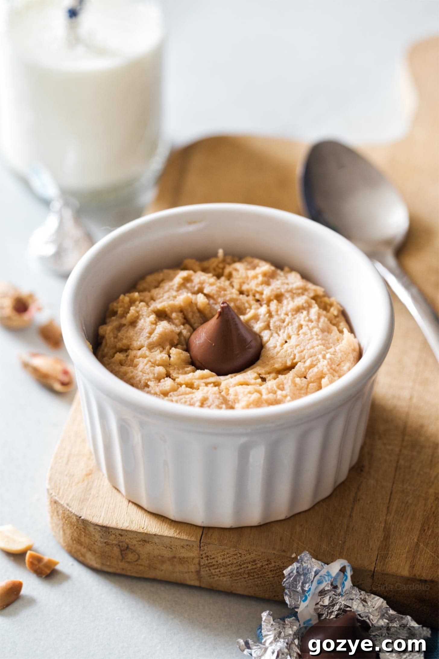 Single-serving peanut butter cookie in a white mug topped with a beautifully melted Hershey's kiss, creating a luscious peanut butter blossom effect.