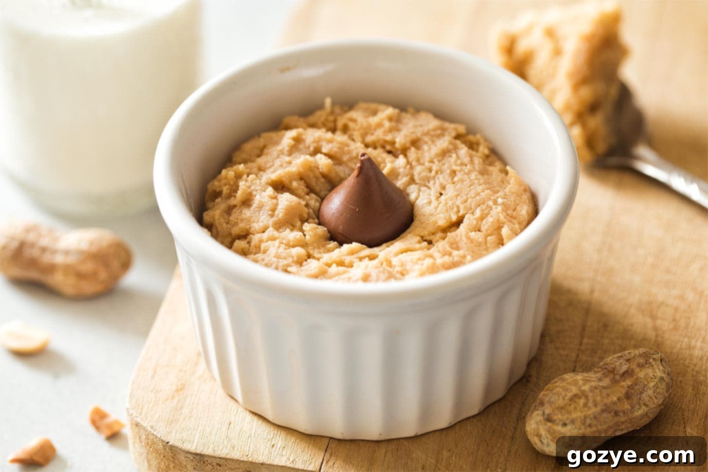 A single-serving peanut butter cookie in a white ramekin, adorned with a perfectly melted Hershey's kiss on top, ready for a delicious bite.