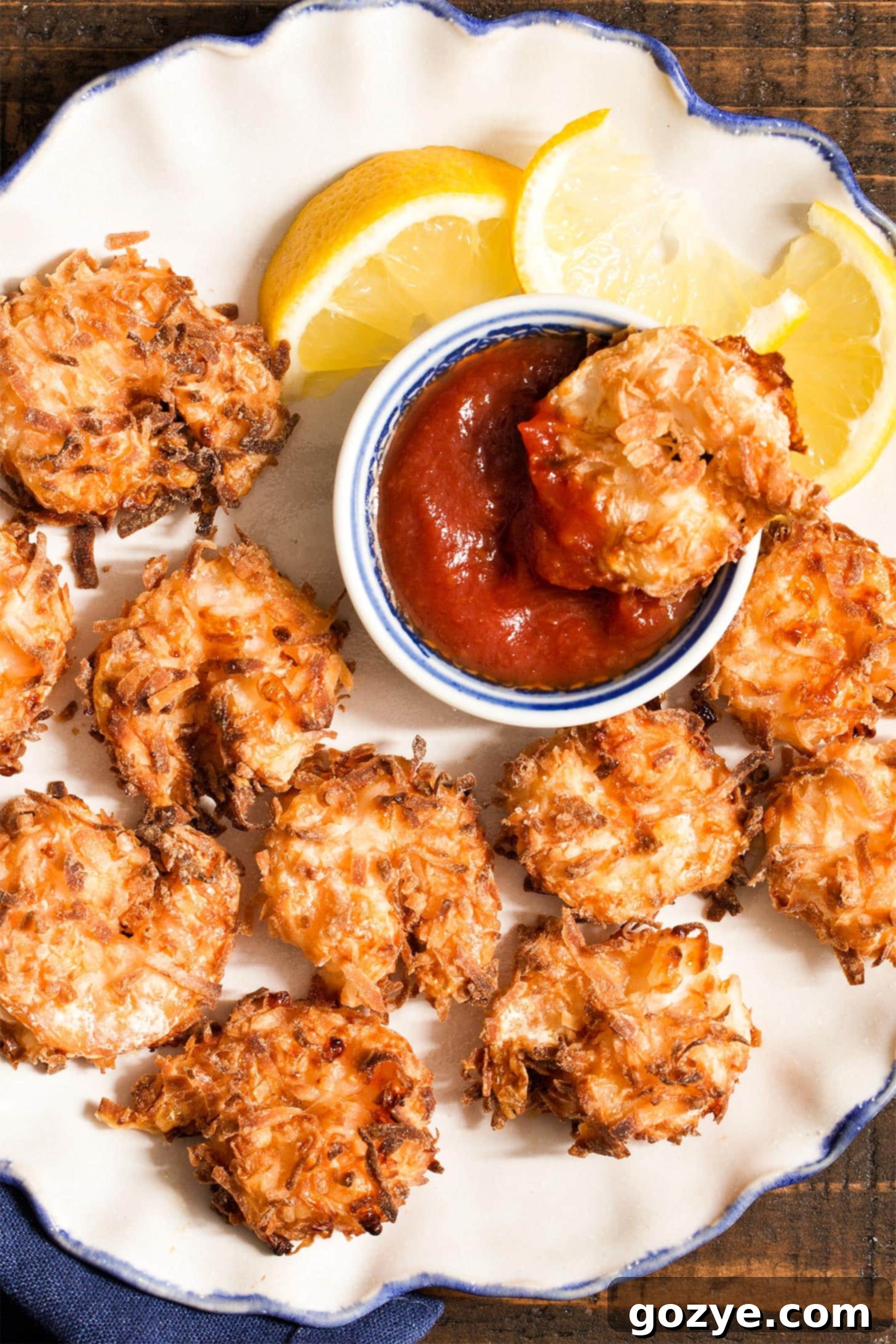 Air fryer coconut shrimp on white ruffled plate with cocktail sauce