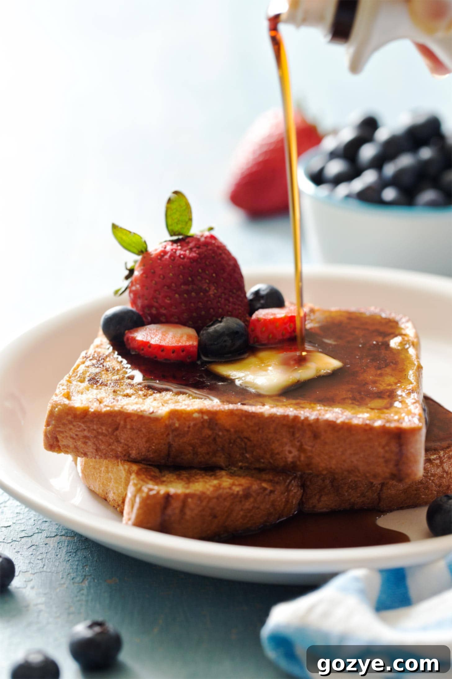 Pouring maple syrup on top of French toast for two with fresh berries
