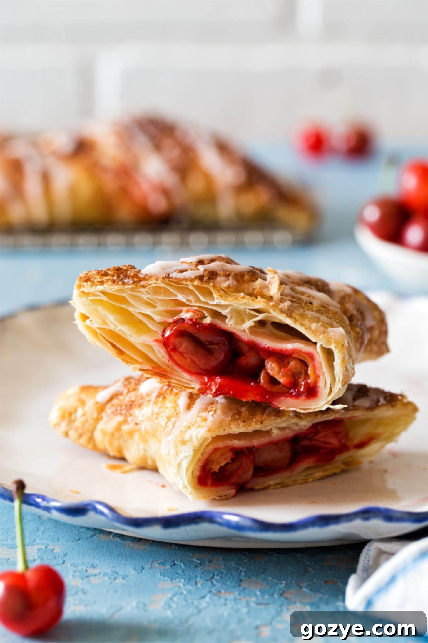 Stacked Cherry Turnovers made with flaky puff pastry on a white plate, garnished with a vanilla glaze