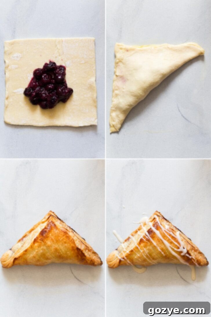 Hands carefully folding a square of puff pastry diagonally over a dollop of blueberry pie filling to form a triangle turnover shape on a lightly floured surface.