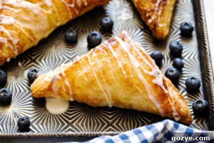 A close-up view of a single blueberry puff pastry turnover on a cookie sheet, highlighting its textured, flaky crust and golden hue.