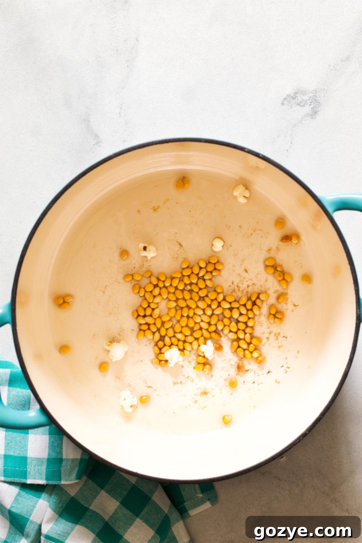 A hand gently shaking a pot on the stove, where oil and a few popcorn kernels are heating, illustrating the 'test pop' phase.