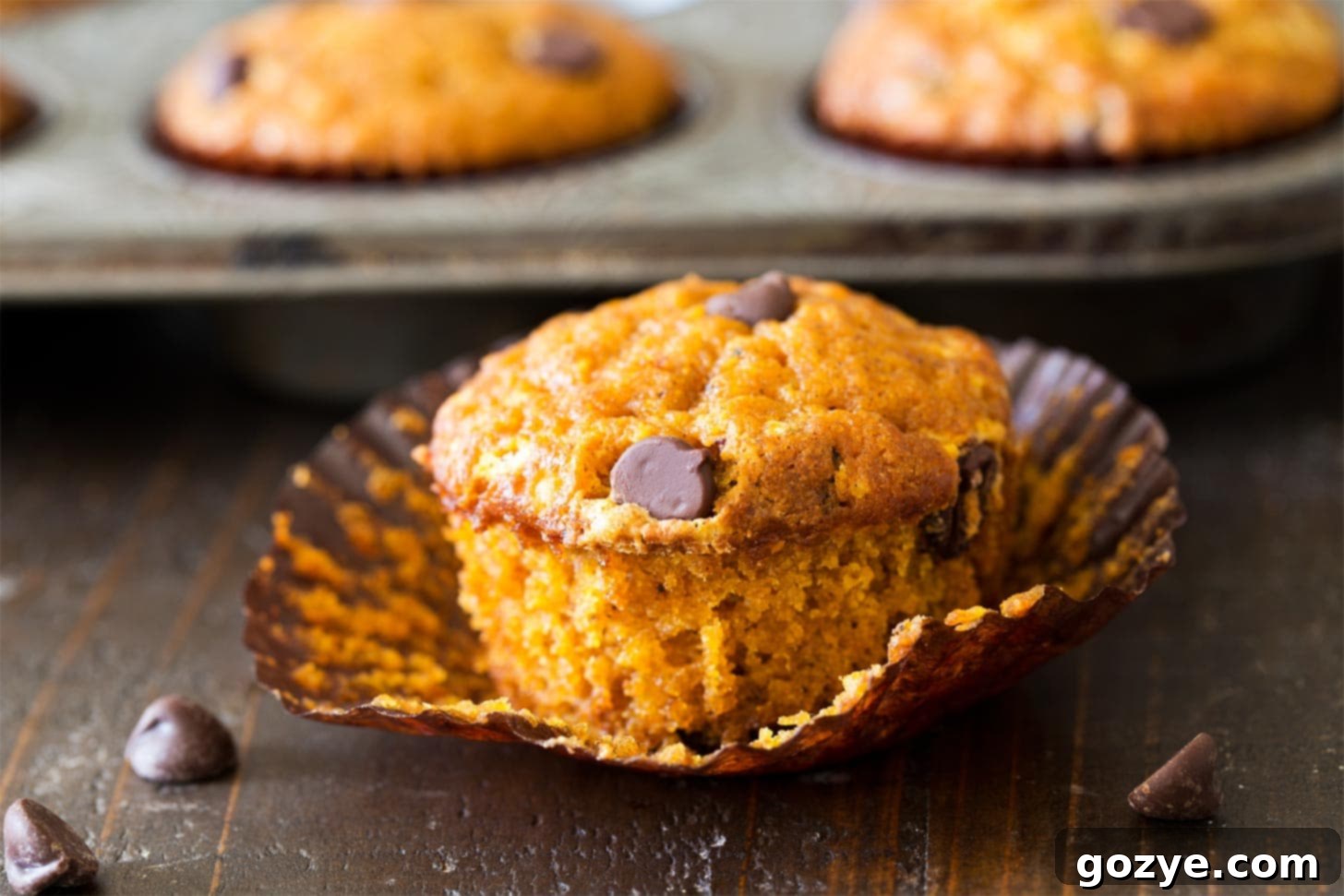 An unwrapped pumpkin spice muffin on a white surface