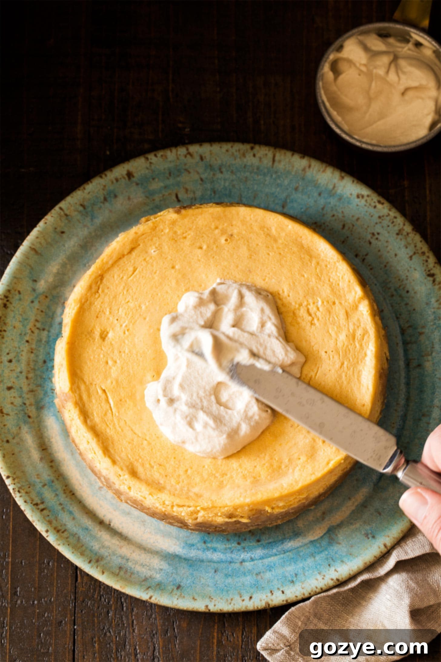 Spreading smooth maple whipped cream generously on top of a delicious small pumpkin cheesecake