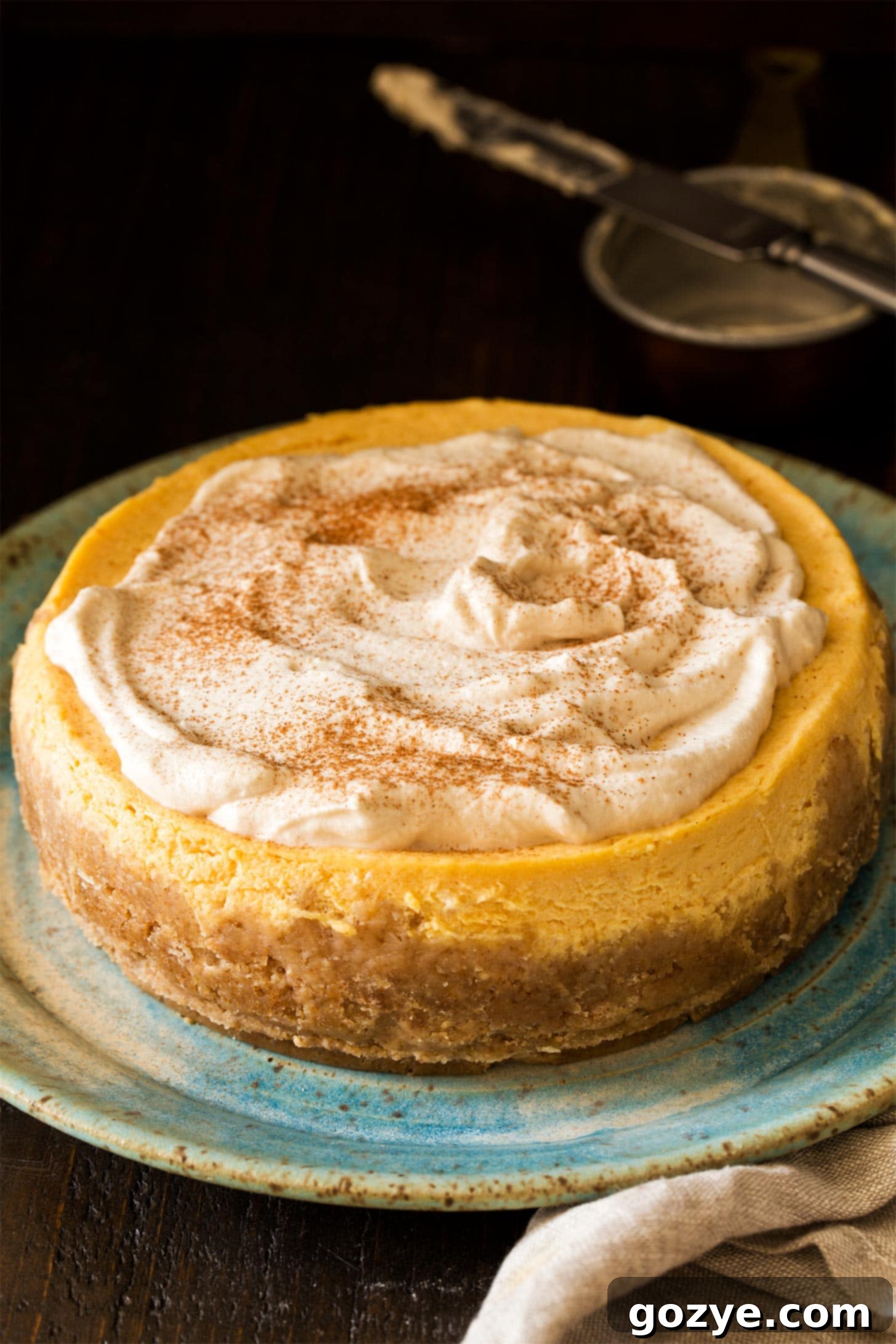 A whole Instant Pot Pumpkin Cheesecake garnished with a generous swirl of maple whipped cream, ready to be served.