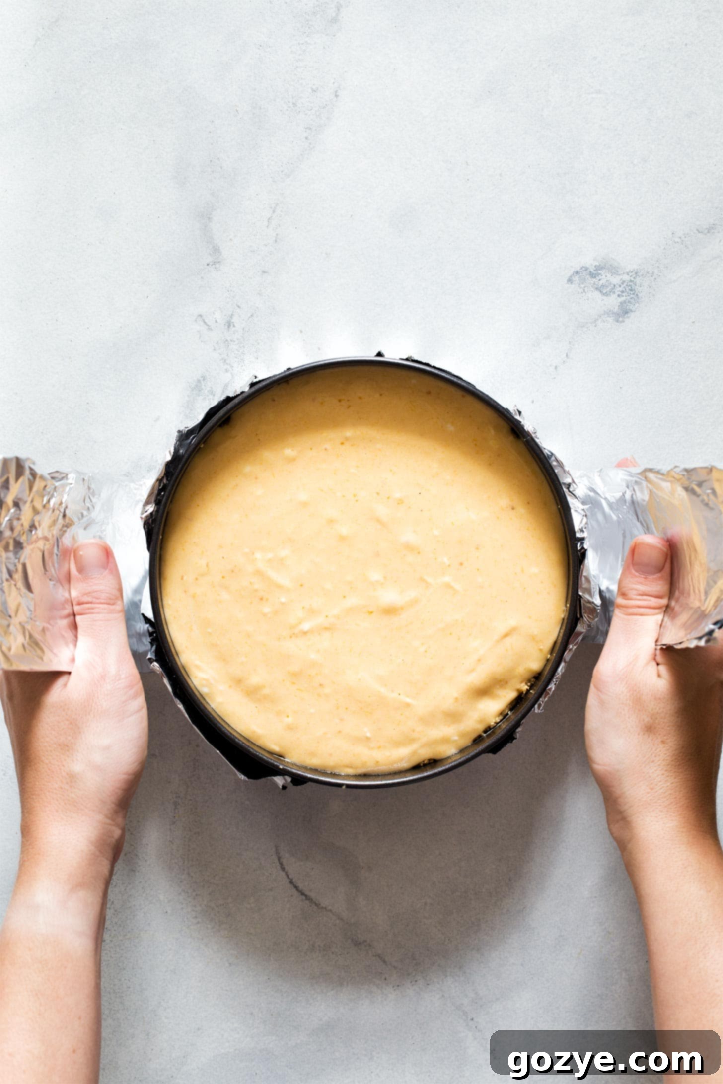 Close-up shot of a person using a foil sling to carefully lift an Instant Pot Pumpkin Cheesecake out of the pressure cooker, demonstrating the removal technique.