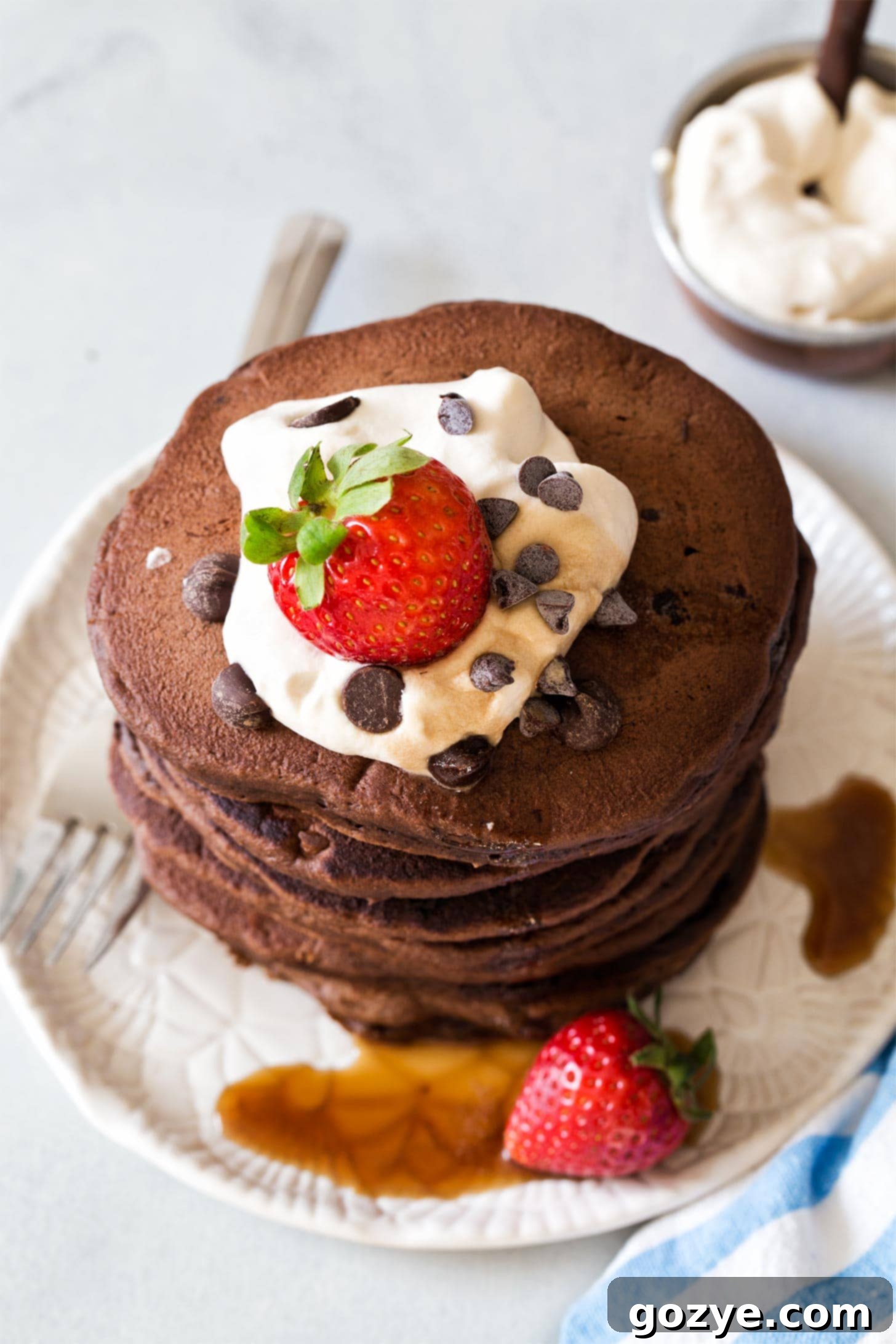 A stack of warm double chocolate pancakes generously topped with maple whipped cream and fresh strawberries