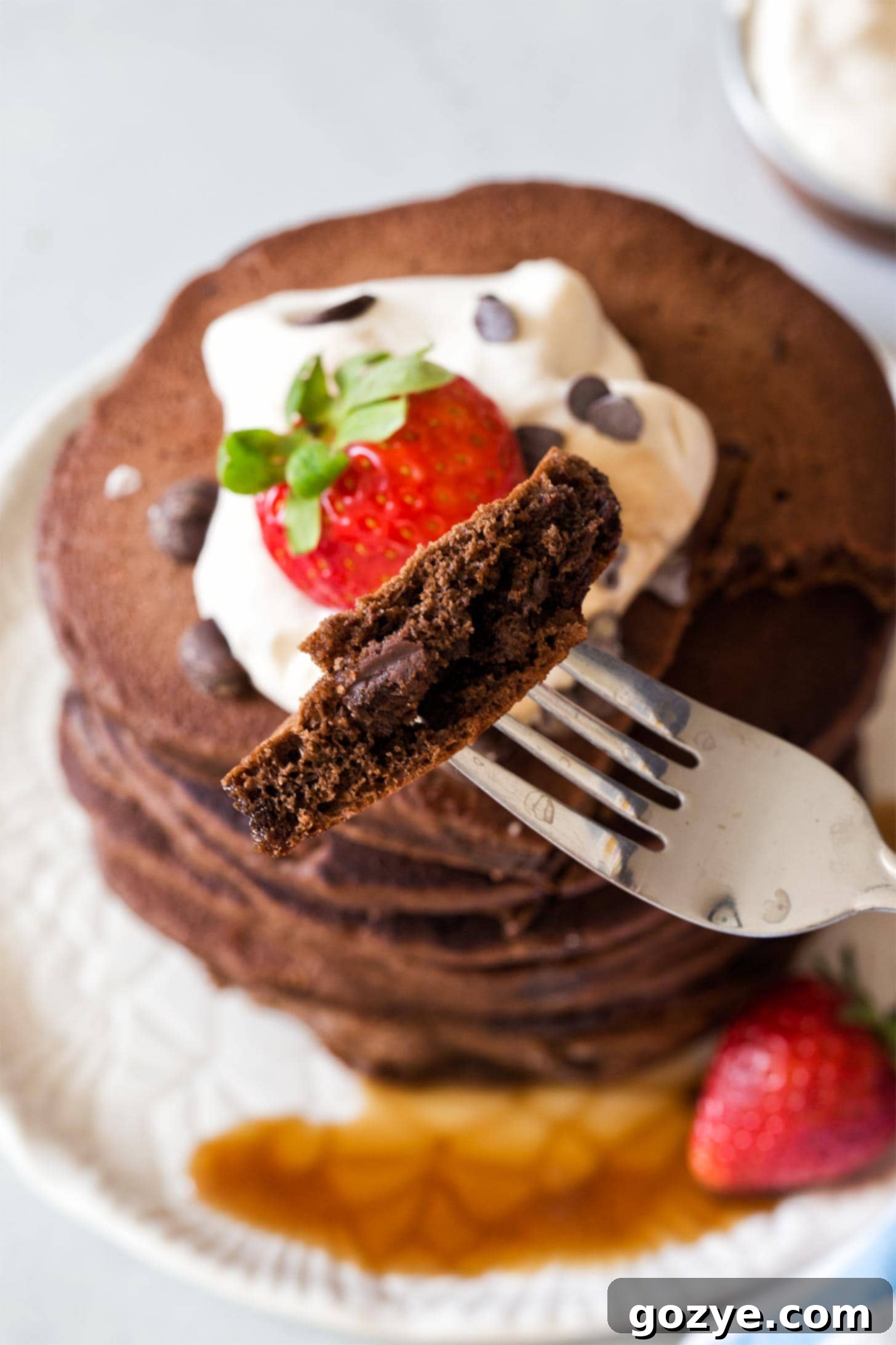 A fork taking a bite from a fluffy chocolate pancake, revealing the melted chocolate chips inside
